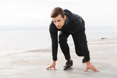 Handsome confident young sportsman working out at the beach, ready to start running, posingの写真素材