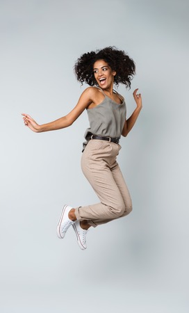 Full length of a happy young african woman casually dressed jumping isolated over gray background