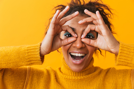 Cheerful young african woman wearing sweater standing isolated over yellow background, showing okの写真素材