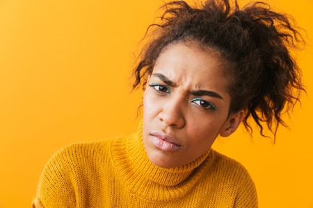 Upset young african woman wearing sweater standing isolated over yellow background