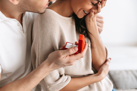 Cropped image of a happy young man making a proposal to his girlfriend with a ring in a box at homeの写真素材