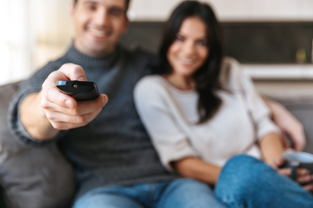 Happy young couple sitting on a couch at home, watching TV, drinking teaの写真素材