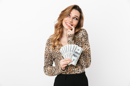 Beautiful young woman wearing leopard blouse standing isolated over white background, holding money banknotes, looking upの写真素材