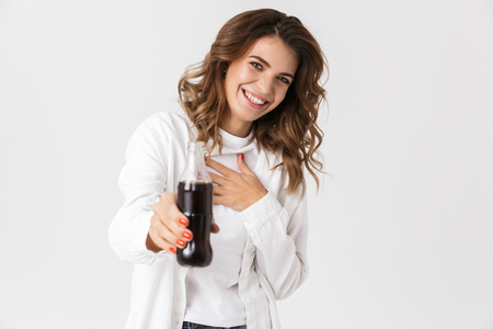 Portrait of cheerful woman in casual clothes holding bottle with soda while standing isolated over white backgroundの写真素材