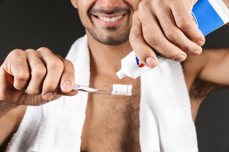 Close up of smiling shirtless man with towel on his shoulders standing isolated over black...