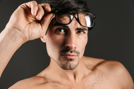 Image of a serious concentrated handsome young man isolated over dark background wearing eyeglasses.の写真素材