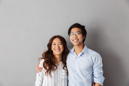 Cheerful asian couple standing over gray background, huggingの写真素材