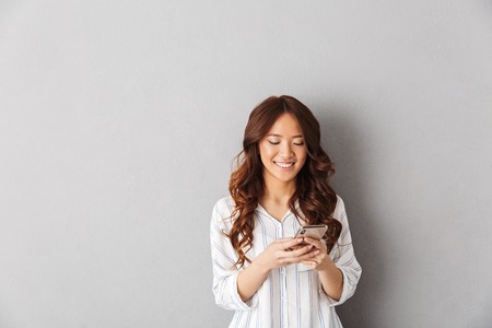 Cheerful asian woman standing isolated over gray backgroundの写真素材