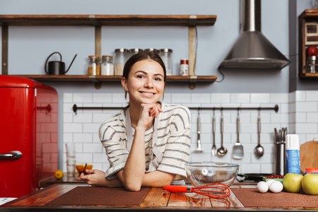 Happy young woman standing at the kitchen at homeの写真素材