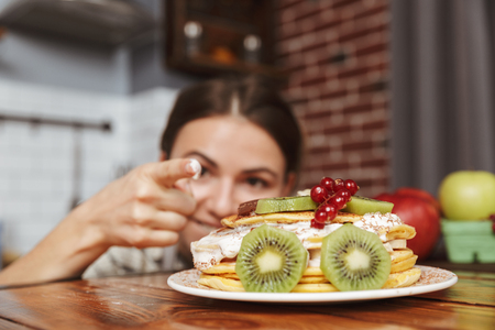 Close up of a woman looking at prepared pancakes with fruits and cream on a tableの写真素材