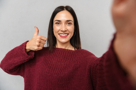 Picture of pretty young woman dressed in burgundy sweater take selfie by camera isolated over grey wall background.の写真素材