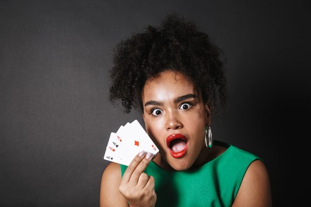 Excited african woman wearing dress showing playing cards isolated over black backgroundの写真素材