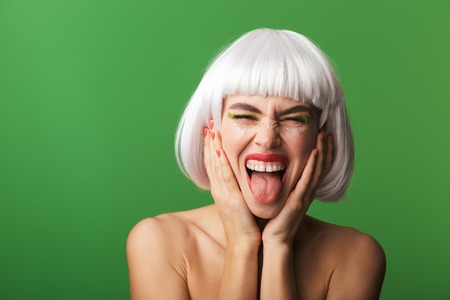 Attractive young topless woman wearing short white hair standing isolated over green background,...