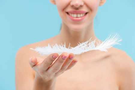 Cropped picture of beautiful young woman posing isolated over blue background holding feather.の写真素材