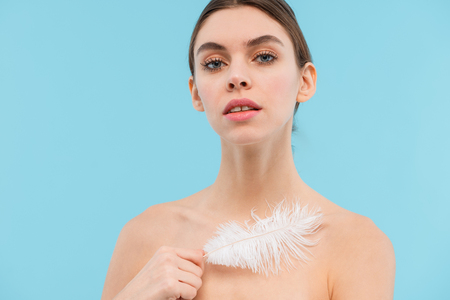 Photo of beautiful young woman posing isolated over blue background holding feather.の写真素材