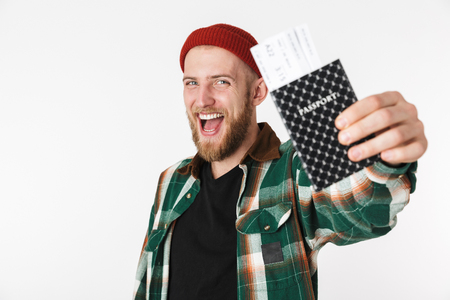 Portrait of happy guy wearing hat and plaid shirt holding passport and travel tickets while standing isolated over white backgroundの写真素材
