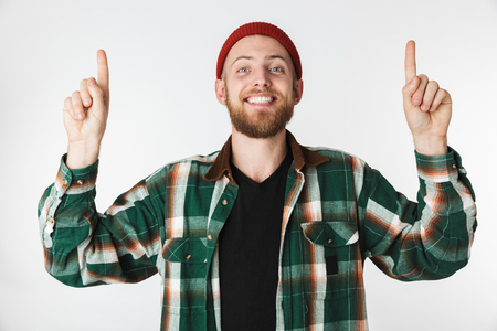 Portrait of handsome man wearing hat and plaid shirt smiling while pointing fingers upward isolated over white backgroundの写真素材