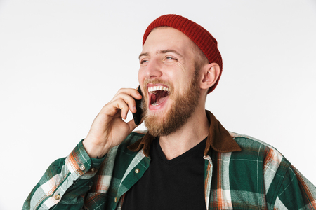 Image of positive guy wearing hat and plaid shirt talking on cell phone while standing isolated over white backgroundの写真素材