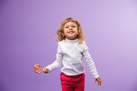 Cheerful little girl holding Christmas lollipop isolated over violet backgroundの写真素材
