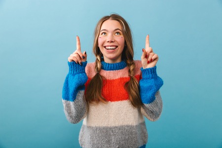Cheerful girl wearing sweater standing isolated over blue backgroundの写真素材