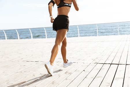 Cropped image of a young sports fitness woman running at the beach outdoors.