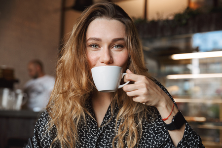 Photo of beautiful young pretty woman sitting in cafe indoors drinking coffee.の写真素材