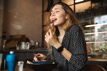 Photo of excited beautiful young pretty woman sitting in cafe indoors have a breakfast.の写真素材
