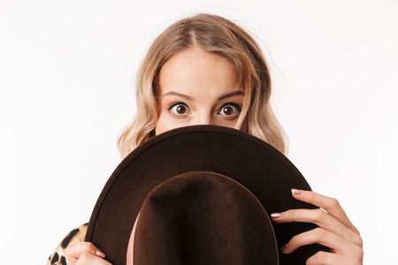 Image of a beautiful young woman covering face with hat isolated over white wall background.の写真素材