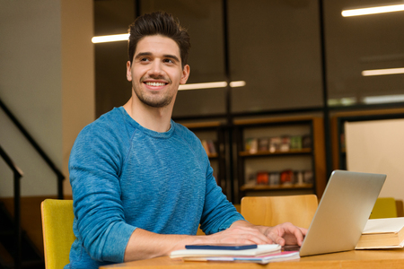 Image of a young student happy man in library doing homework studying read and using laptop computer.の写真素材