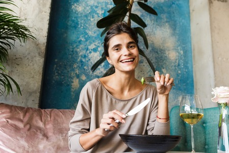 Photo of pretty beautiful young woman sitting in cafe indoors drinking white wine eat salad.の写真素材