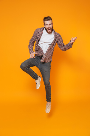 Full length portrait of a cheerful young man wearing casual clothes isolated over yellow background, jumpの写真素材