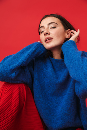 Photo of a beautiful young woman posing isolated over red wall background.の写真素材