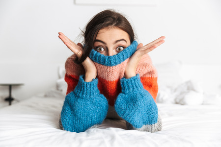 Photo of amusing woman 20s wearing sweater lying in bed at homeの写真素材