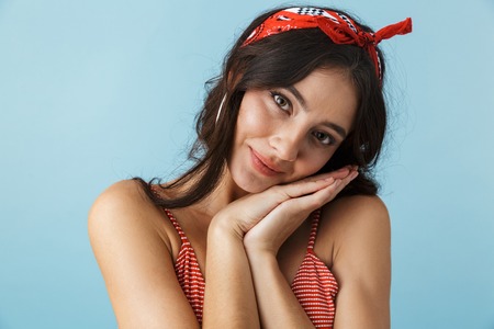 Lovely cheerful girl wearing summer clothes standing isolated over blue background, arms folded at her cheekの写真素材