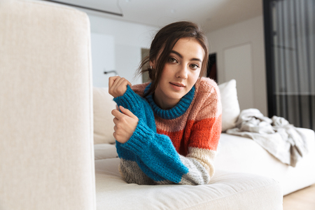 Photo of adorable woman wearing sweater lying on couch in apartmentの写真素材