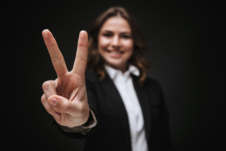 Portrait of a confident young businesswoman wearing formal suit standing isolated over black backgroundの写真素材