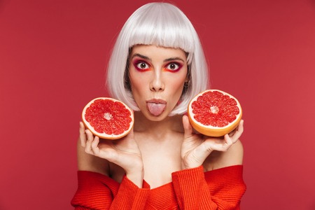 Image of excited funny beautiful young woman isolated over red wall background holding grapefruit.の写真素材
