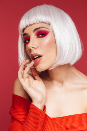 Photo of beautiful young woman isolated over red wall background with bright makeup posing.の写真素材