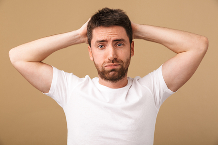 Portrait of a confused young man holding arms on his head isolated over beige backgroundの写真素材