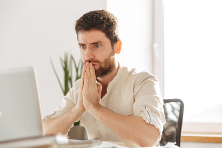 Image closeup of tense businessman 30s wearing white shirt using laptop while working in modern officeの写真素材