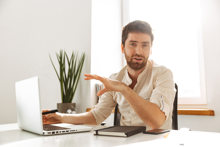 Portrait of attractive businessman 30s wearing white shirt working on laptop while sitting in bright officeの写真素材
