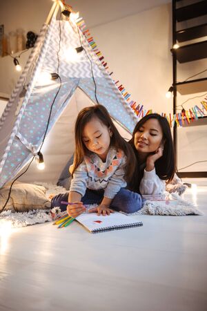 Happy mother and her little daughter playing inside childrens tent at the bedroom, drawingの写真素材