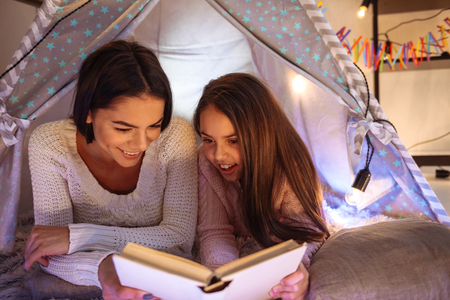 Photo of a happy young woman with her little daughter girl lies on floor reading book. Christmas concept.の写真素材