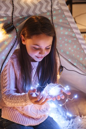 Photo of a happy young little girl on floor holding lights. Christmas concept.