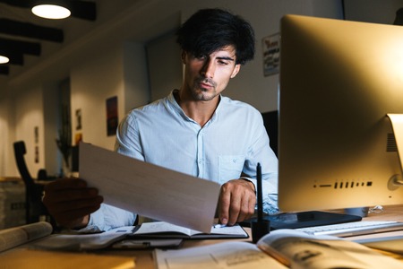 Portrait of a confident concentrated businessman working at the office late at night, examining...