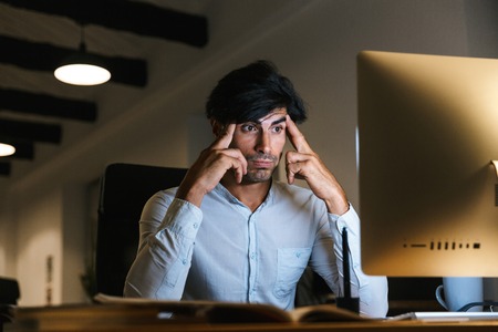 Portrait of a confident concentrated businessman working at the office late at night, having a headacheの写真素材