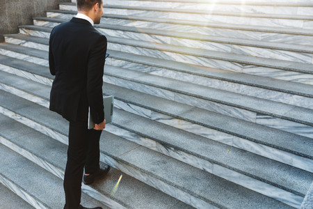 Cropped photo of handsome young businessman walking by steps outdoors at the street holding clipboard.の写真素材