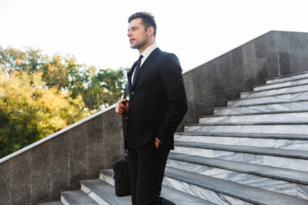 Image of handsome young businessman walking by steps outdoors at the street.の写真素材