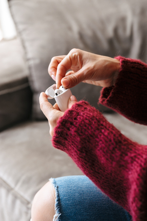 Cropped image of a woman indoors in home on sofa holding case with earphones.の写真素材