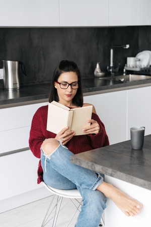 Photo of a pretty woman indoors in home at the kitchen reading book.の写真素材